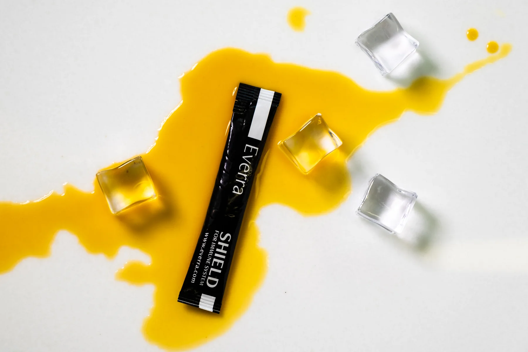 Black cosmetics tube on a splash of yellow liquid with clear and gold cubes