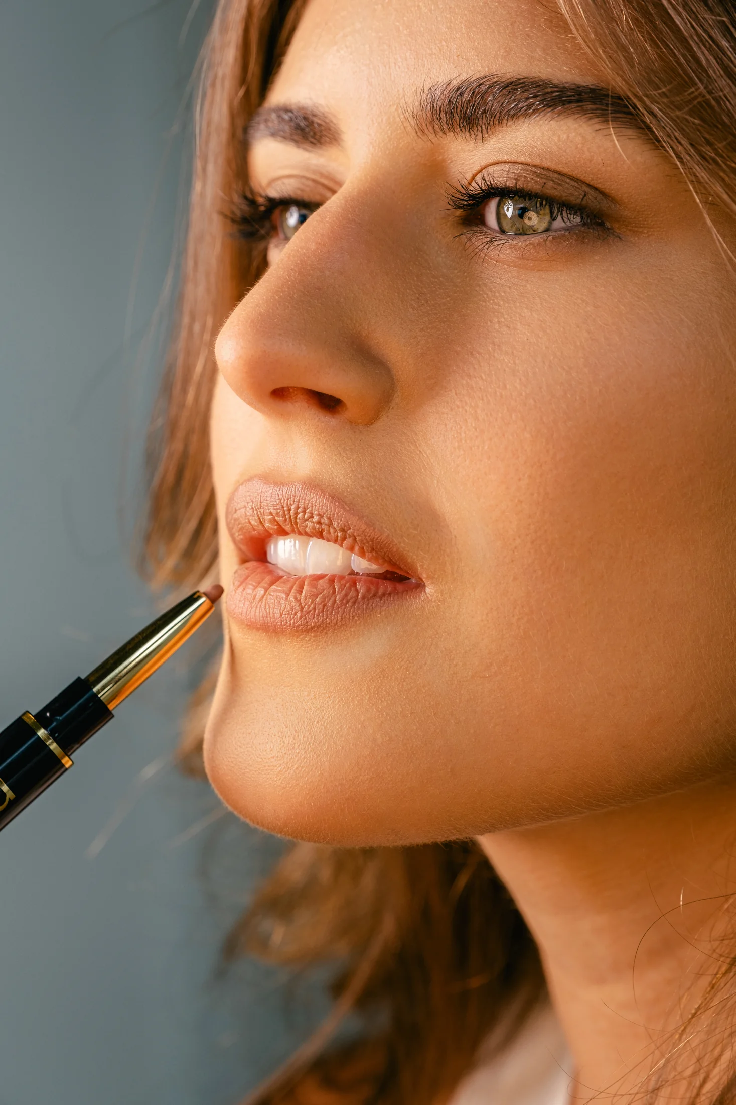 Close-up of a model applying nude lip colour, showing the side of her face