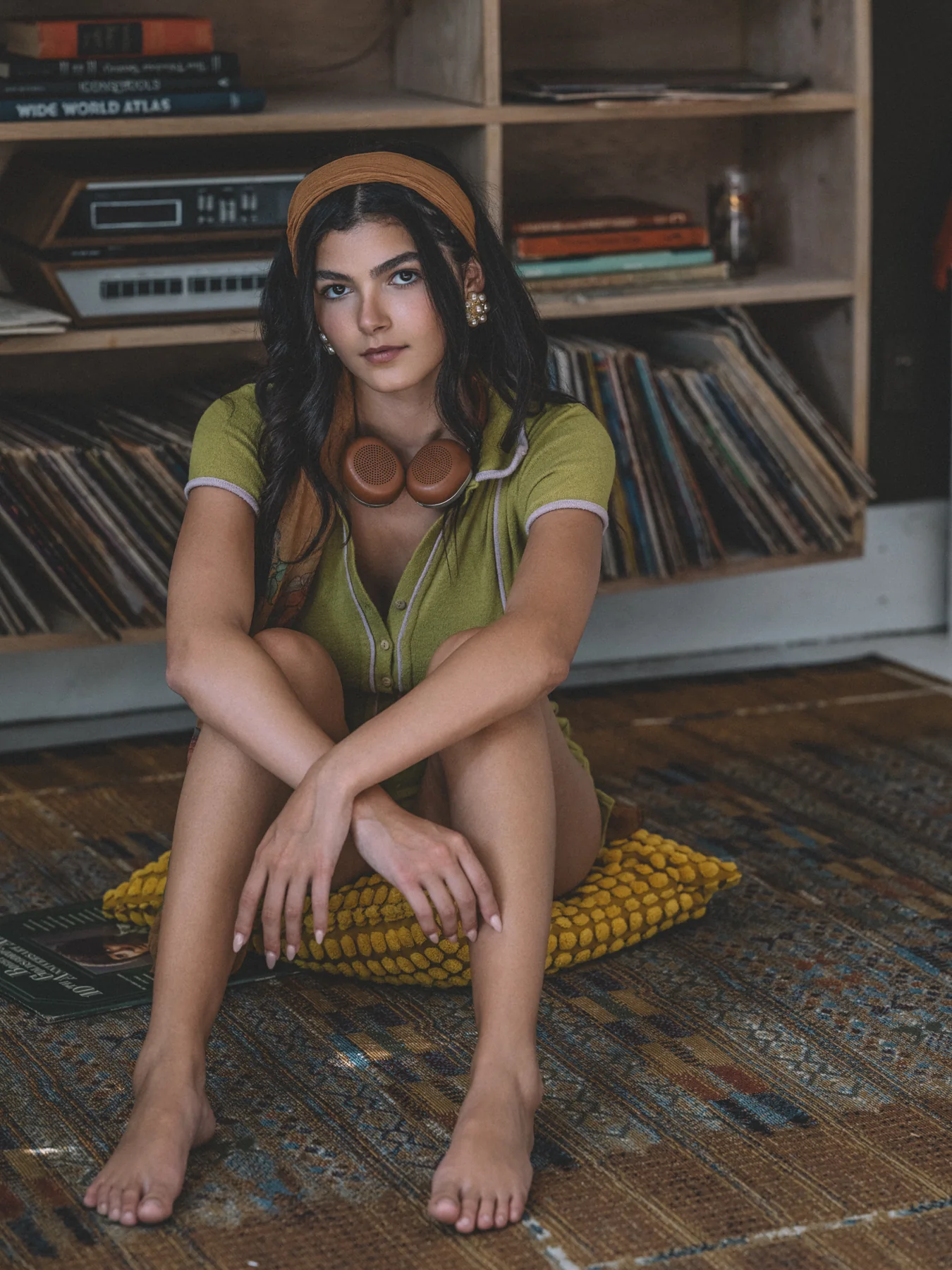Alexis Santiago seated before shelves of records in a green knit outfit and orange headband