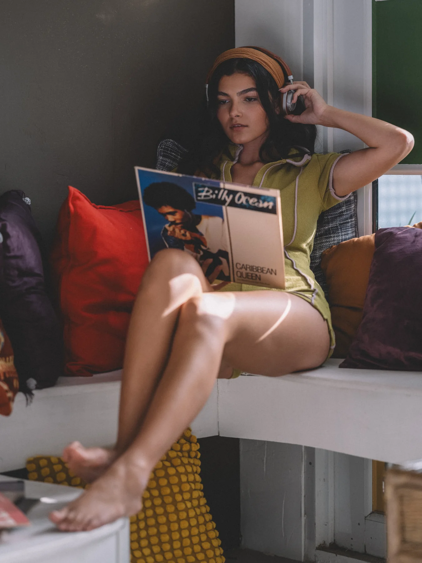 Alexis Santiago wearing headphones and holding a Billy Ocean record beside a window
