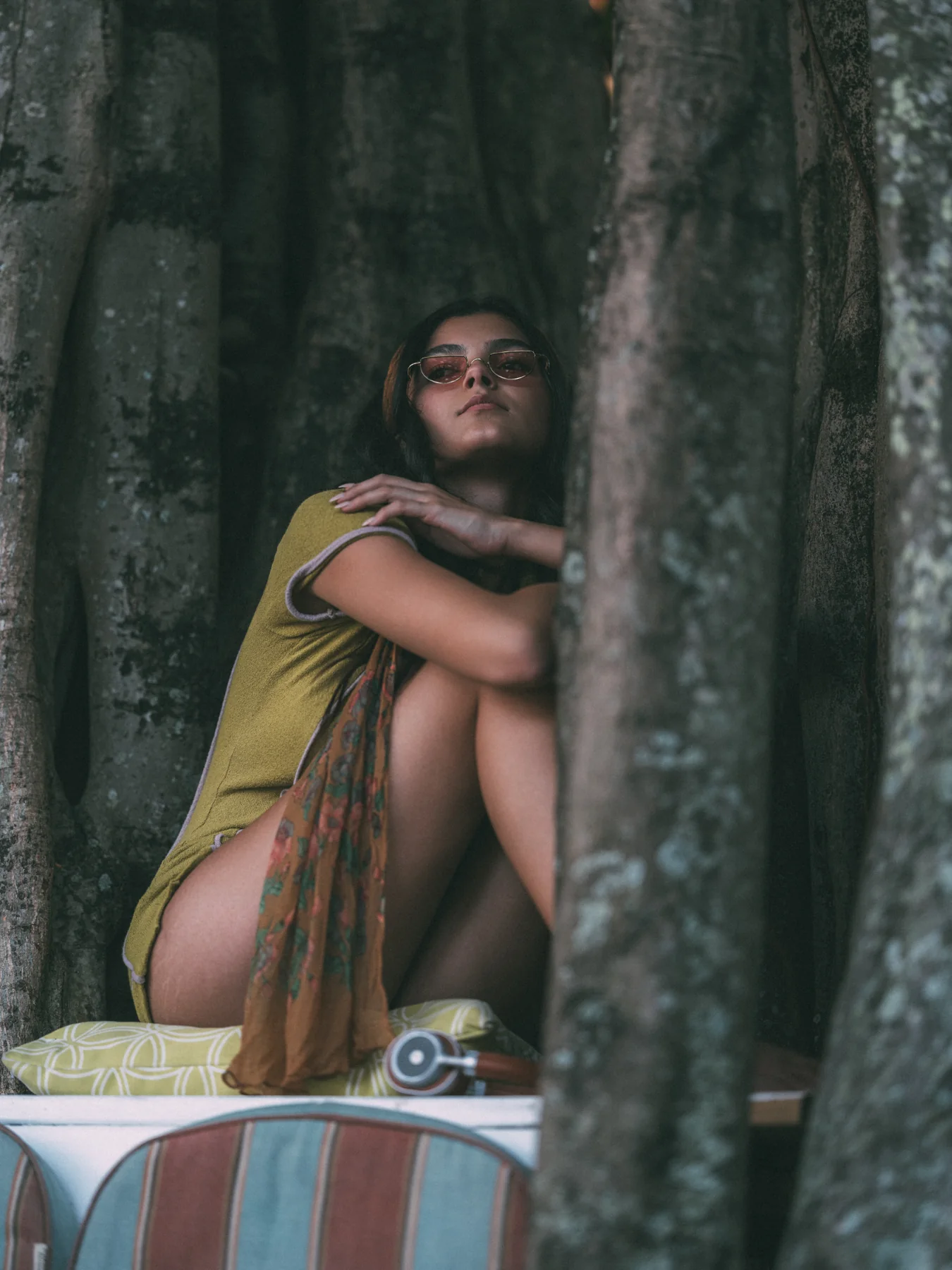 Alexis Santiago in sunglasses seated among tree roots in a green knit outfit