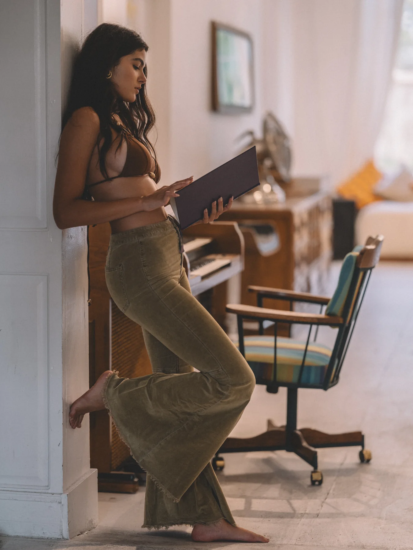 Alexis Santiago in a brown top and olive trousers leaning against a doorway with a record sleeve