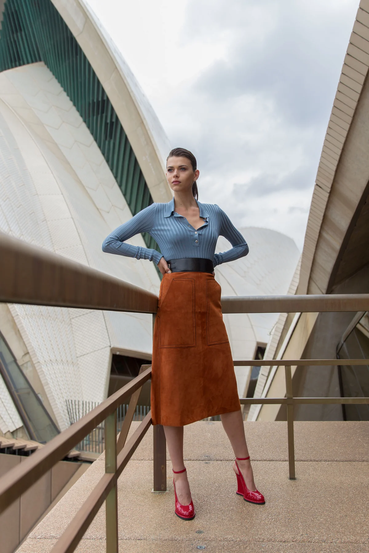 Model in a blue top and rust-coloured skirt on a walkway at the Sydney Opera House