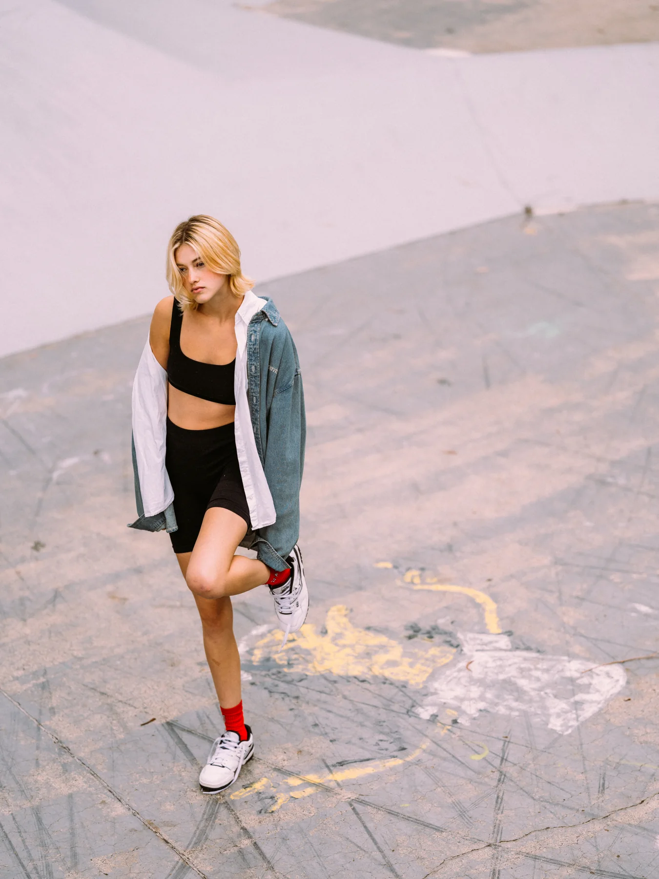 Gracie Rae standing on sloping concrete in an oversized denim shirt and white trainers