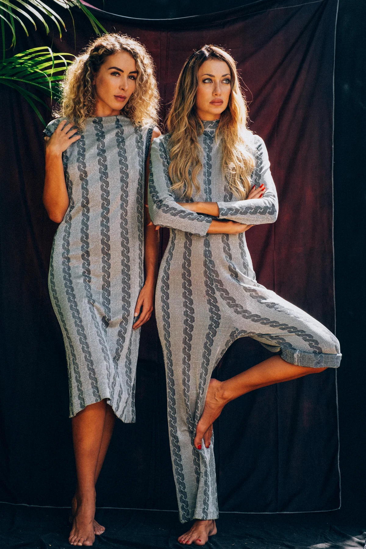 Two models wearing grey patterned dresses against an outdoor fabric backdrop