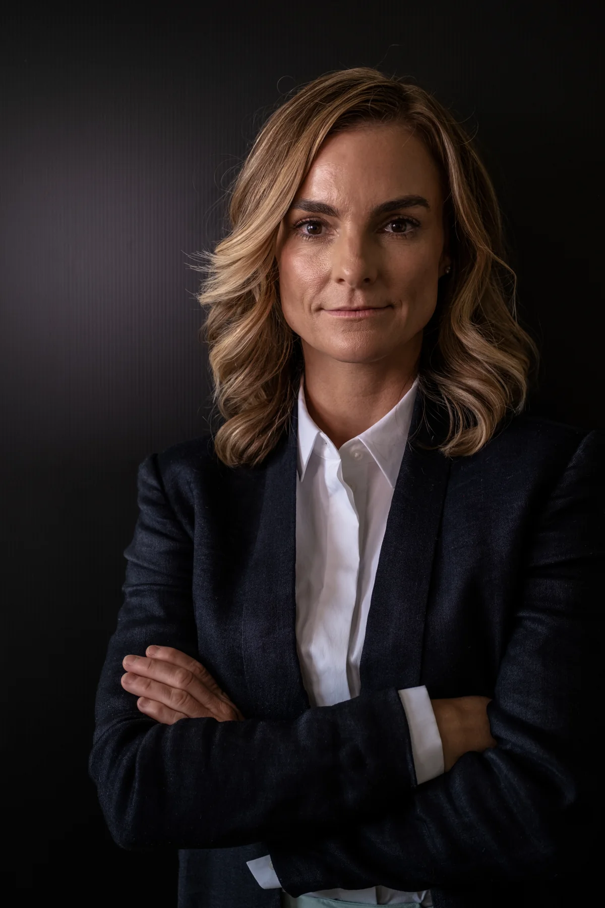 Lindy wearing a white shirt and dark blazer against a dark studio background