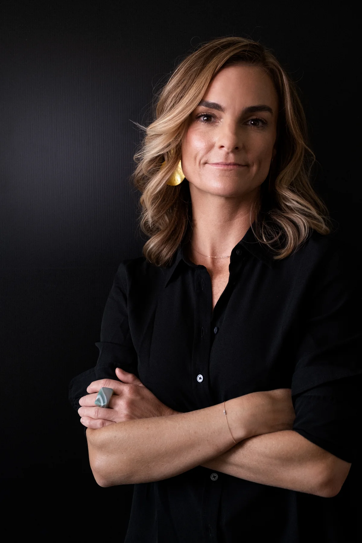 Portrait of Lindy in a black shirt with folded arms against a dark background