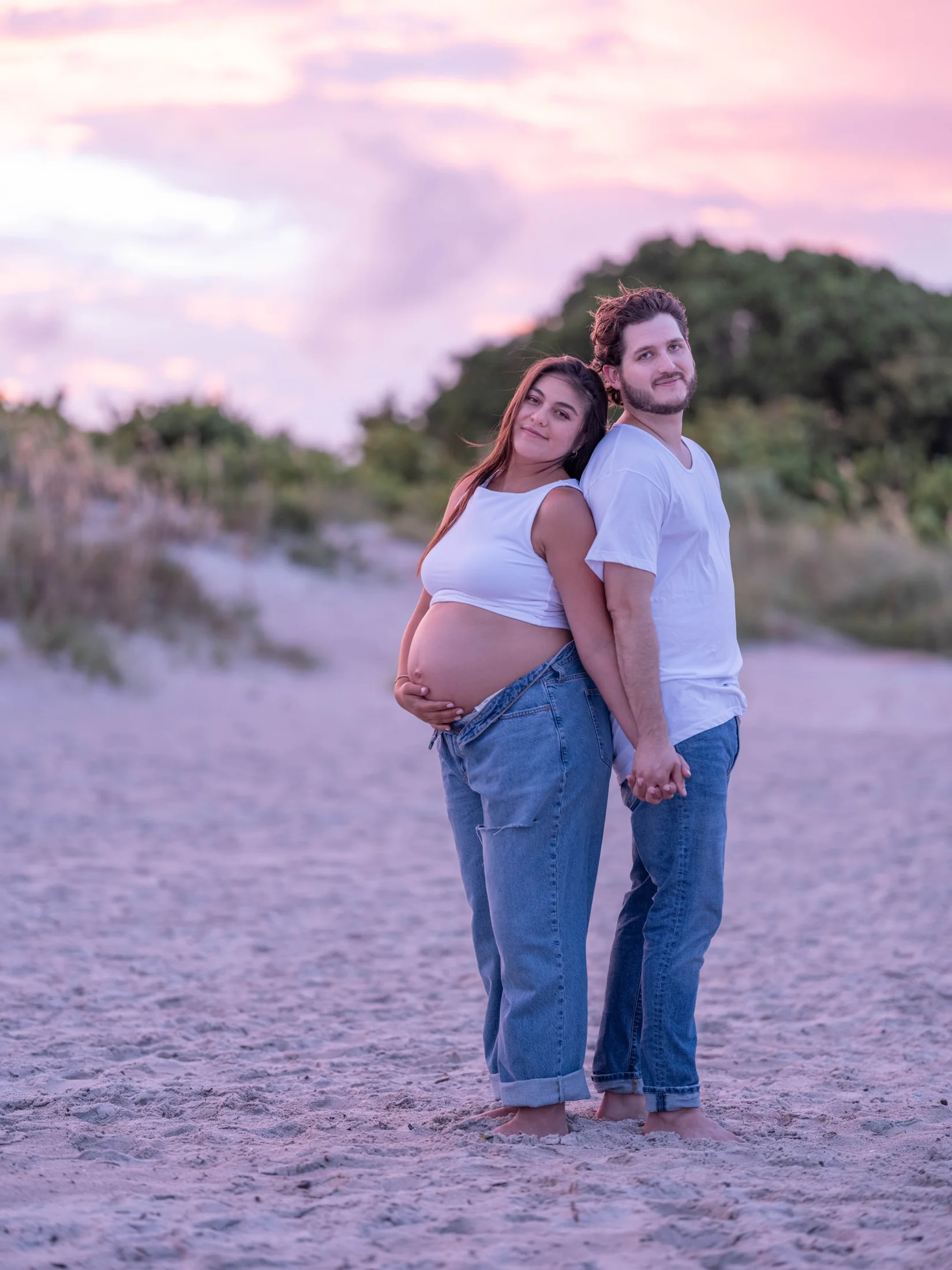 Michelle resting her hands on her bump while leaning against Peter at sunset on the beach