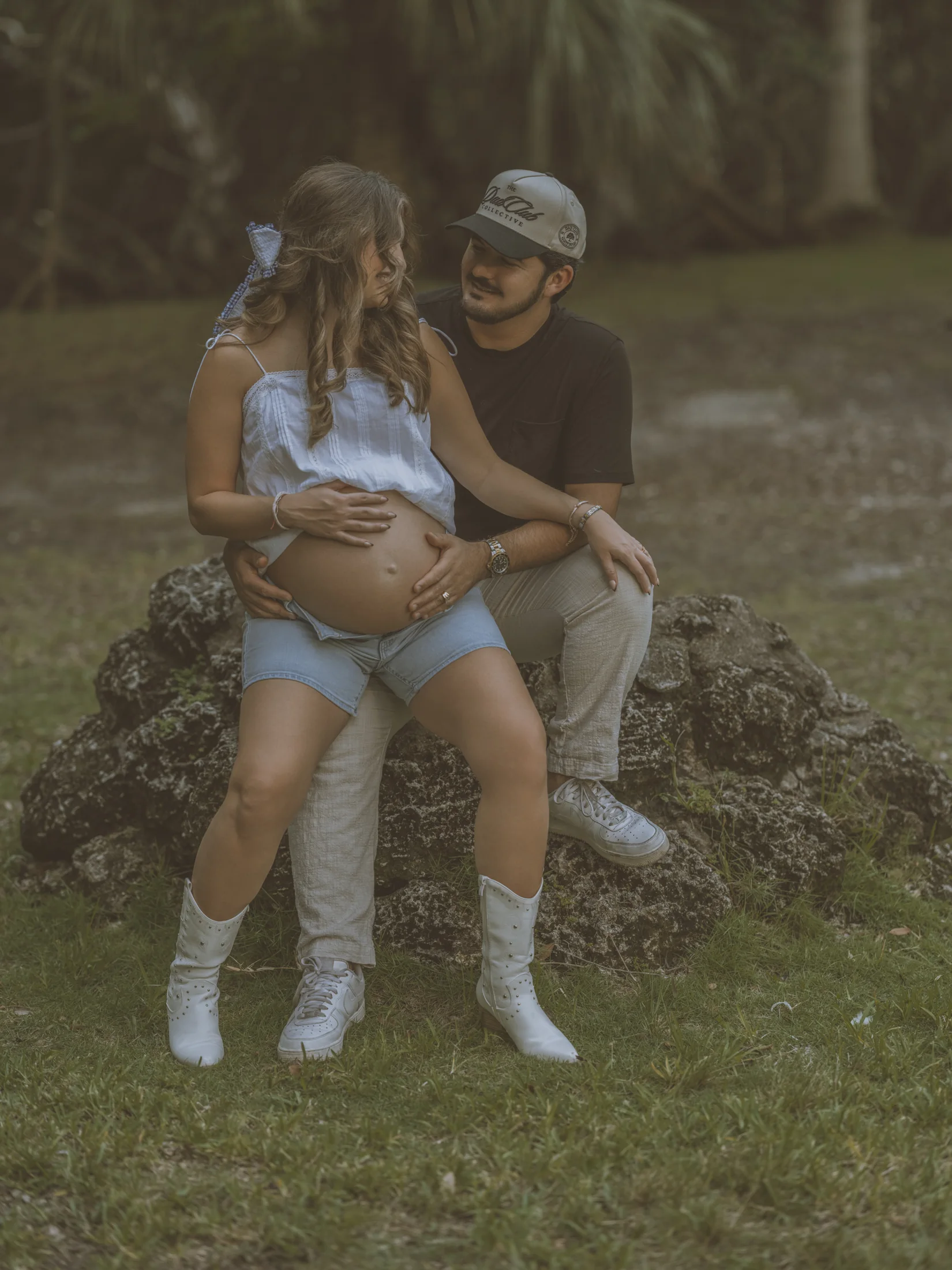 Kelsey and her partner seated together on a rock under the trees