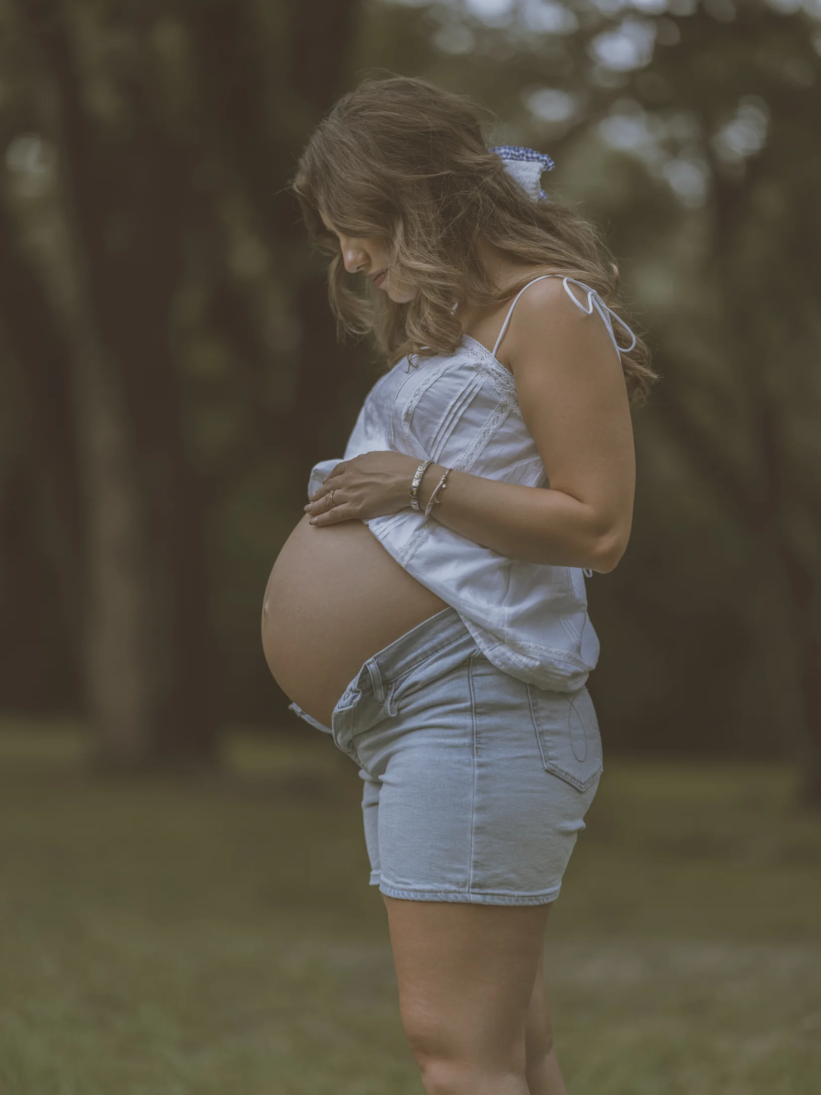Side-on maternity portrait of Kelsey in a pale blue top and denim shorts