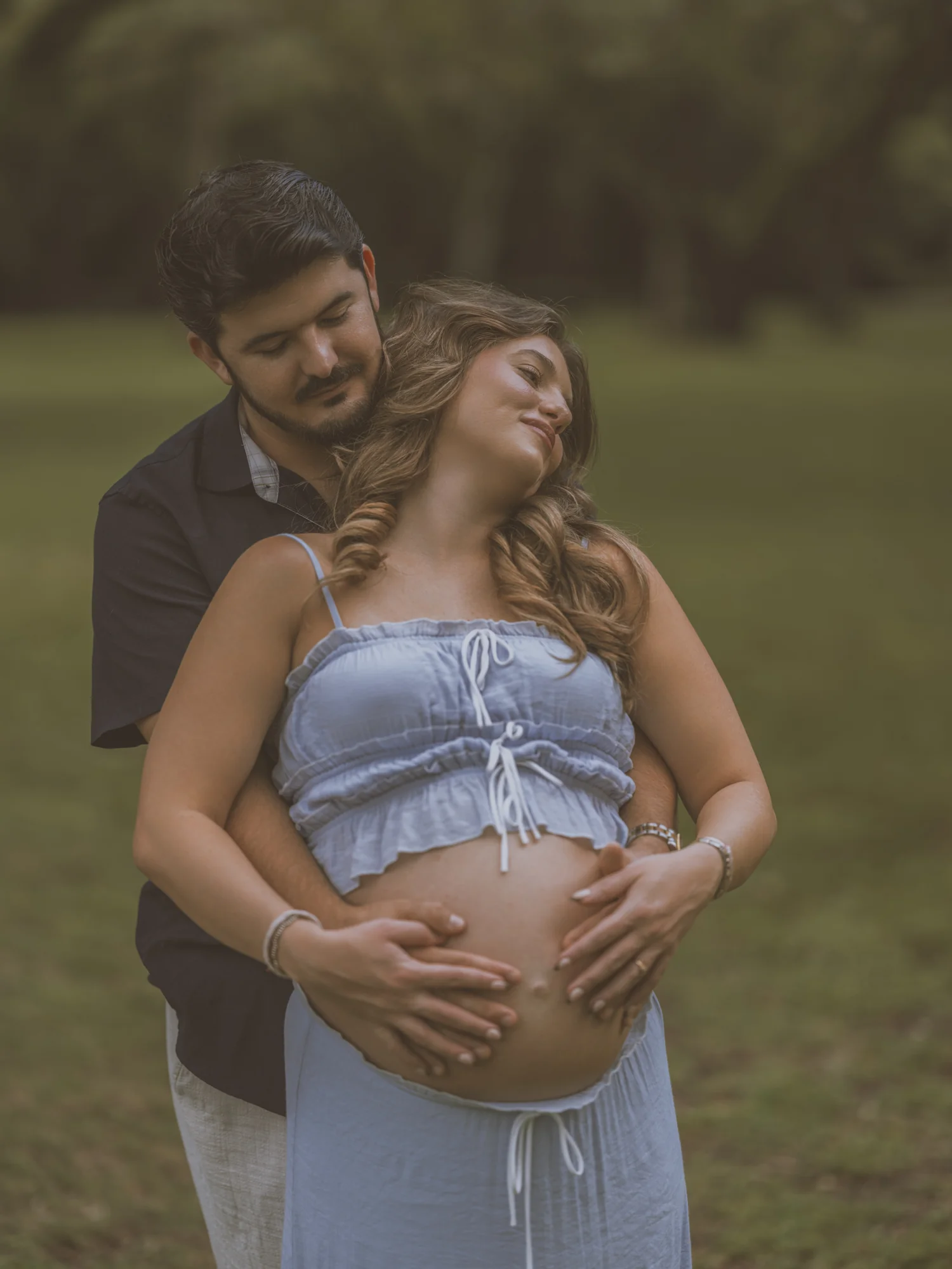 Kelsey and her partner embracing beneath the trees, with their hands on her bump