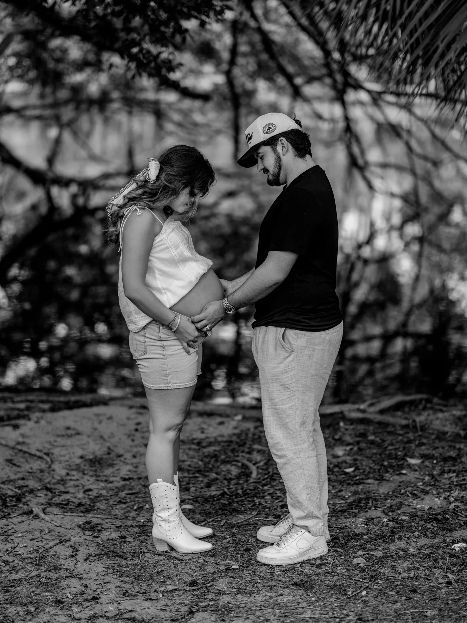 Black-and-white portrait of Kelsey and her partner looking down at her bump