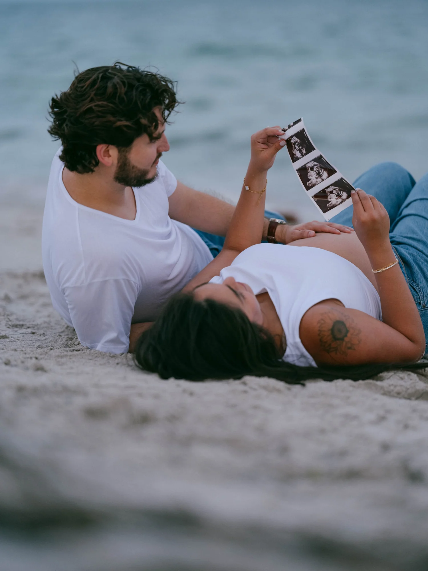 Peter and Michelle lying on the sand looking at ultrasound photographs