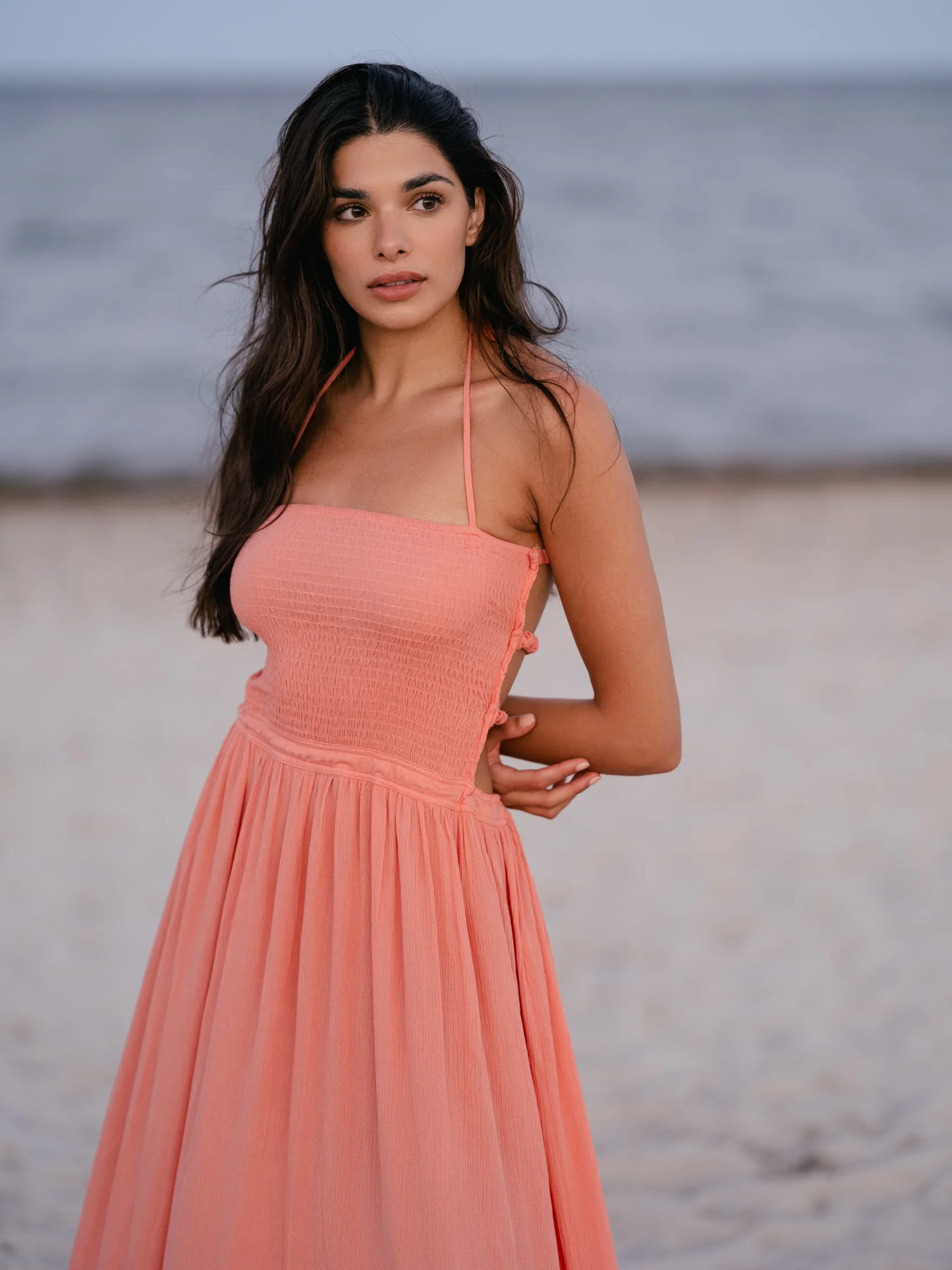 Rhea Rai standing on the beach in a flowing coral dress