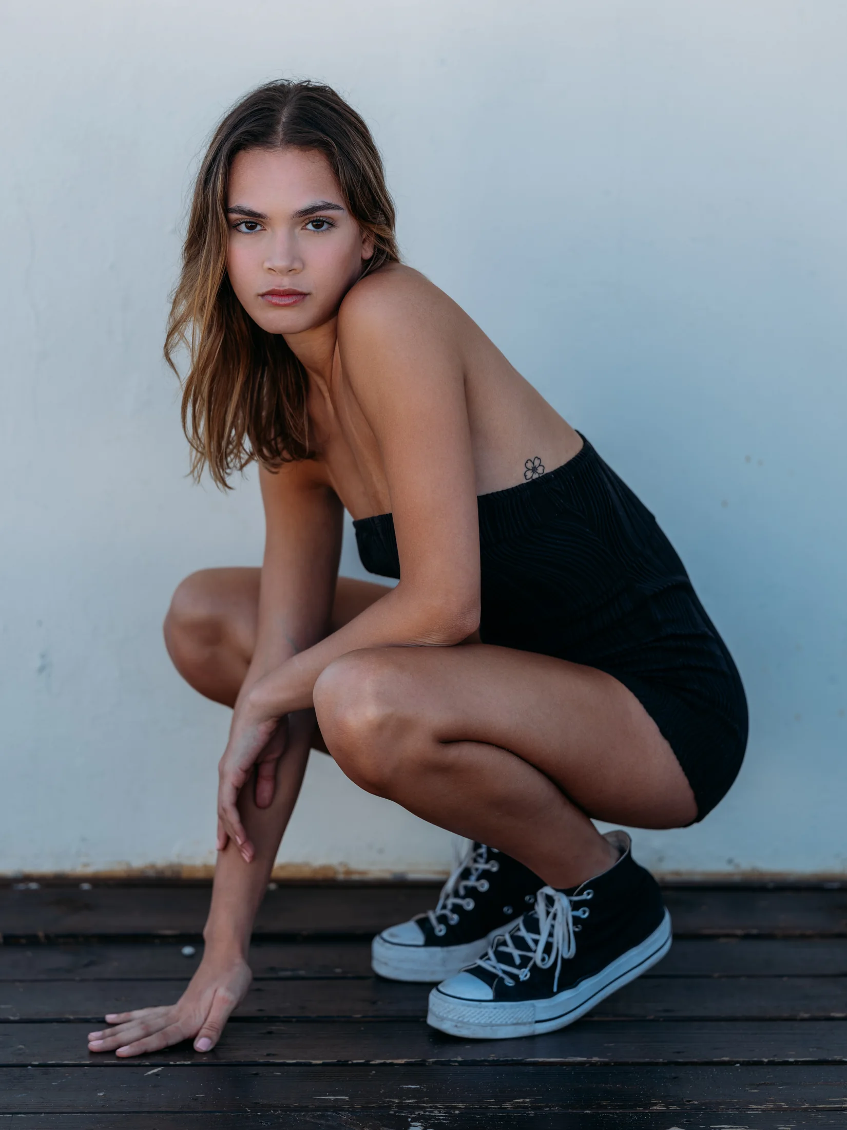 Vianni Mateo crouching on a wooden deck in a black outfit and high-top trainers