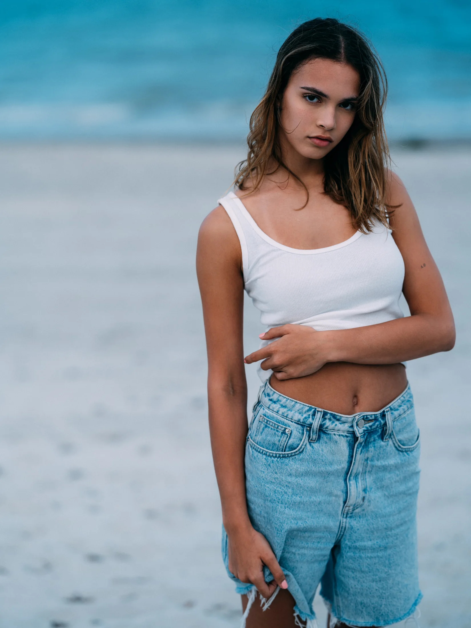 Vianni Mateo in a white vest and denim shorts on the beach