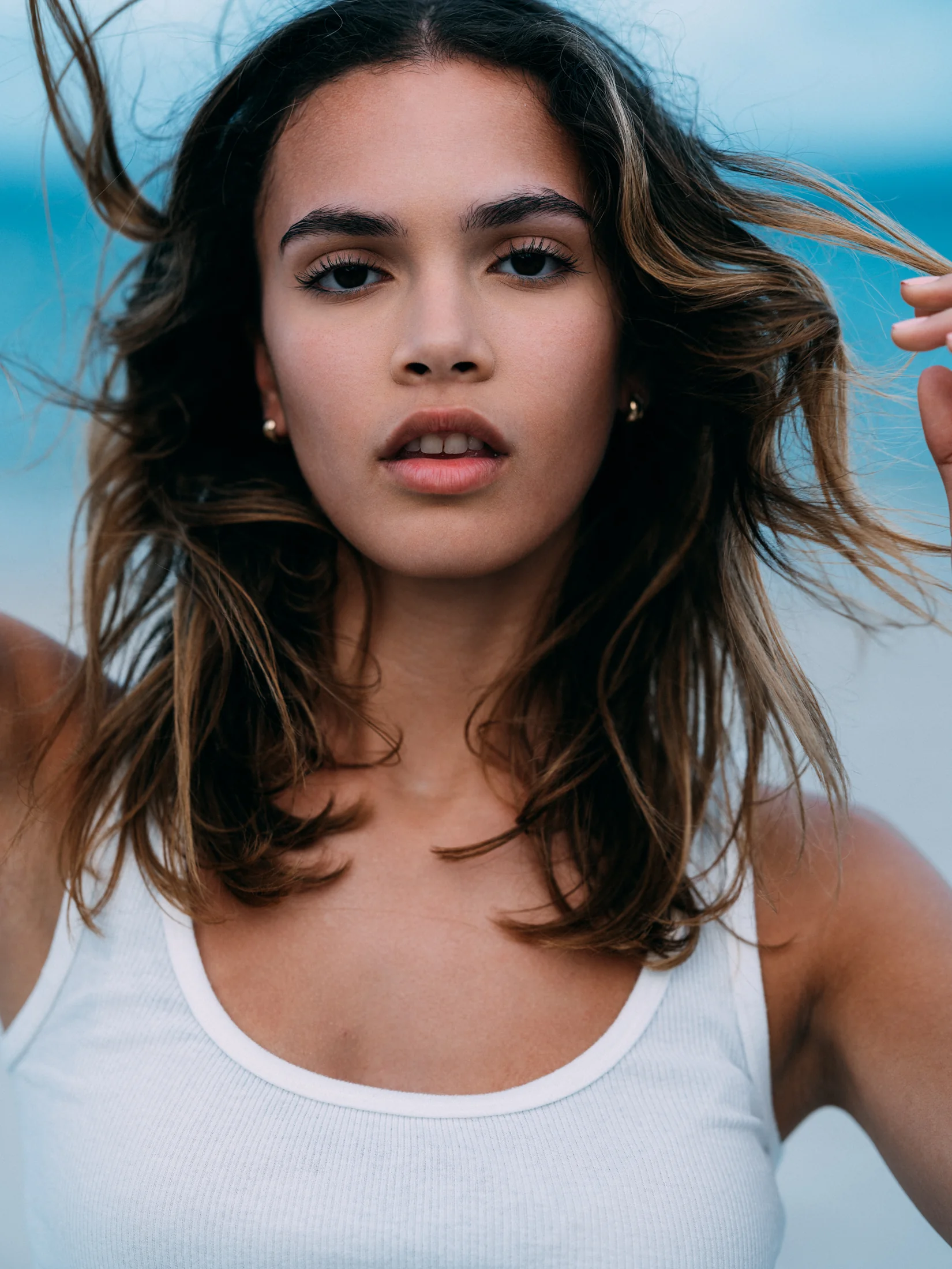 Close-up beach portrait of Vianni Mateo in a white vest with windblown hair