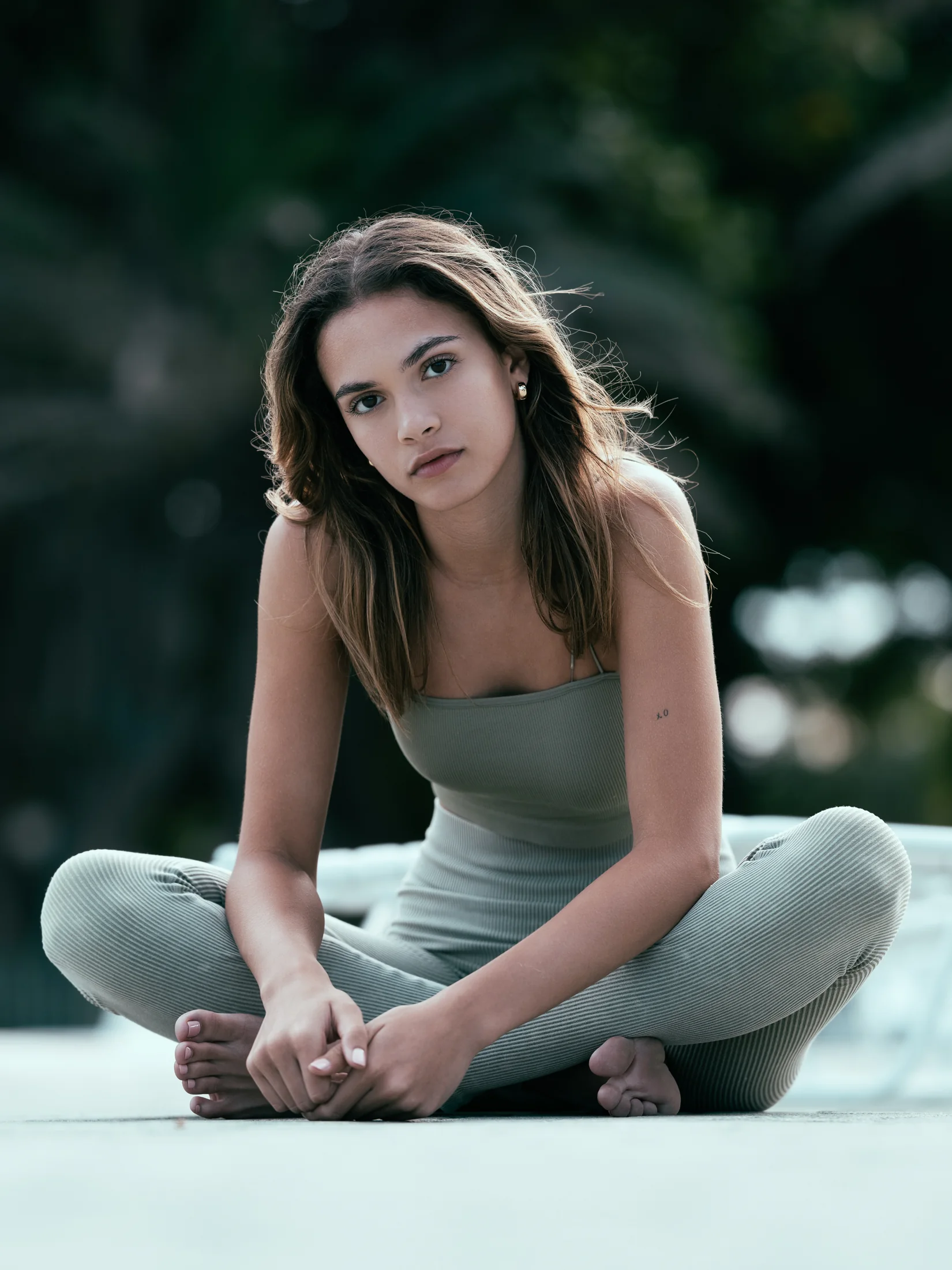 Vianni Mateo seated cross-legged in a sage-green outfit by the pool